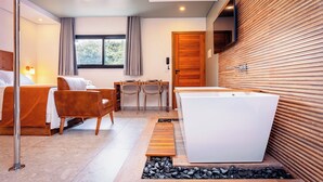A modern hotel room with a bed, a sofa, a dining table with chairs, a bathtub, and a wooden wall. - VELINN 2Secreto Hotel Boutique (Ilhabela)