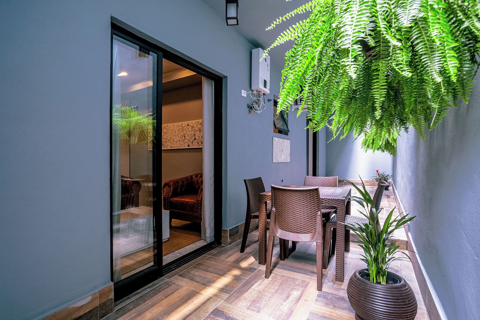 A room with a sliding glass door leading to a balcony, wicker furniture, a potted plant, and a wall-mounted air conditioning unit.