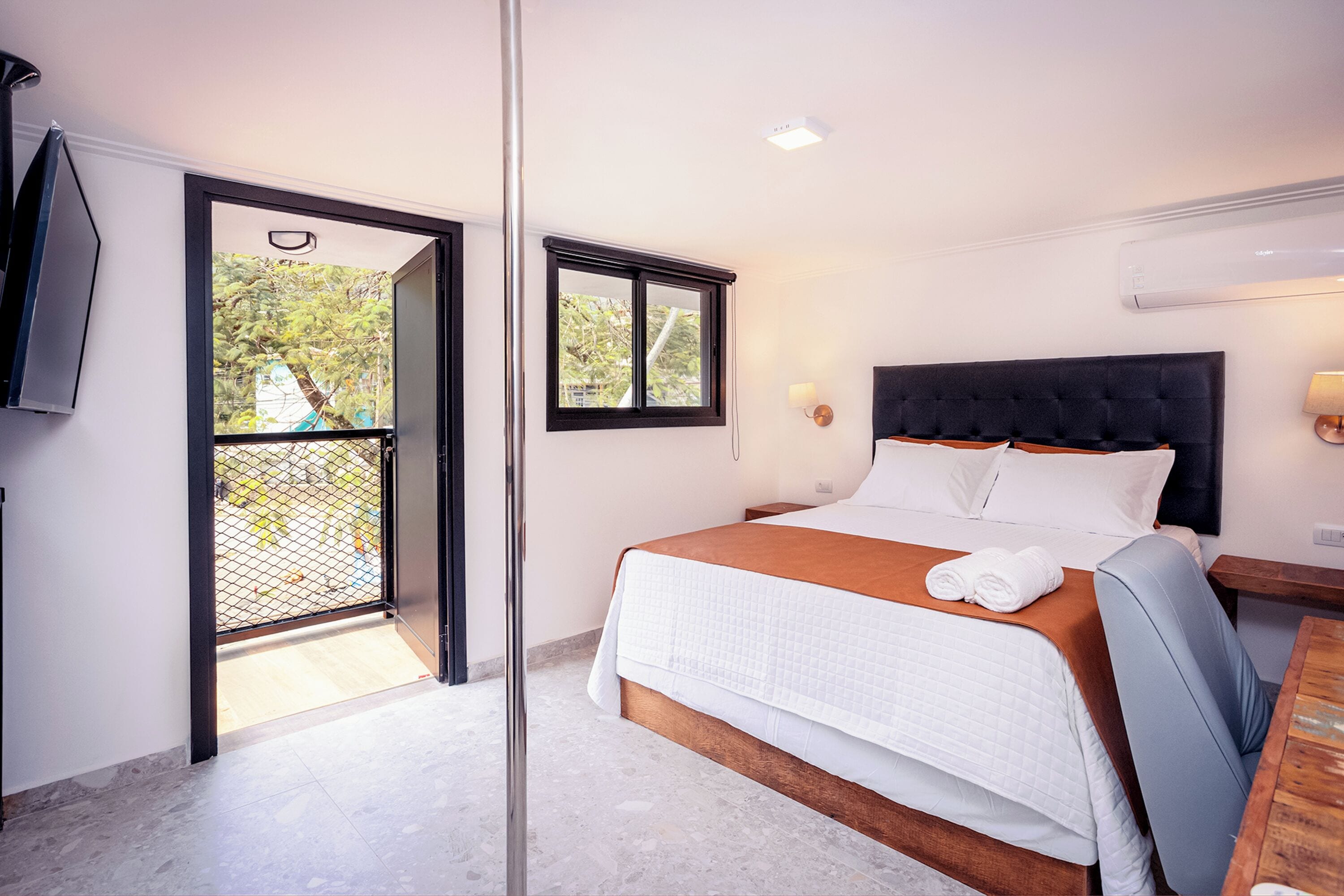 Habitación de hotel con cama, escritorio, silla, televisión y ventana con vistas a árboles.