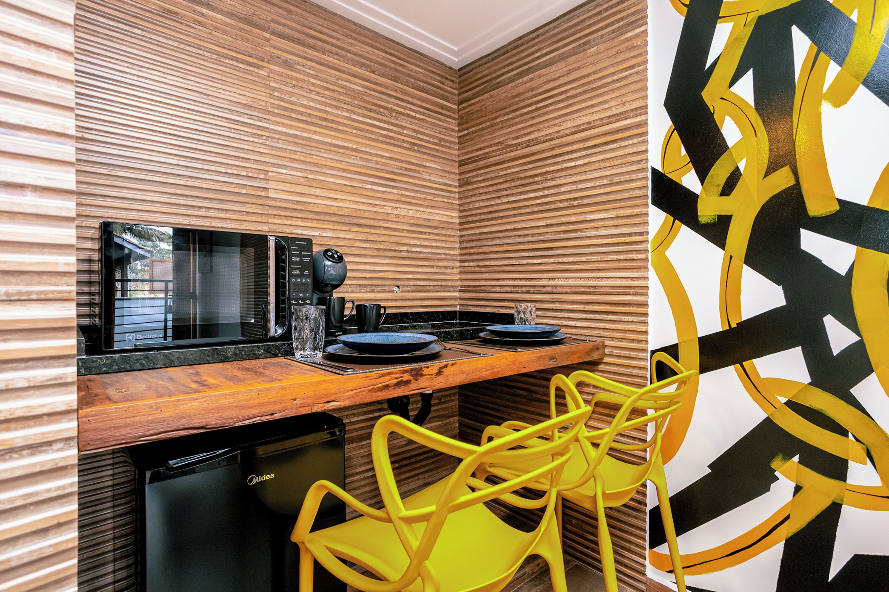 A kitchen with wooden paneling, a microwave, a coffee maker, and a dishwasher. There are two yellow chairs and a black countertop.