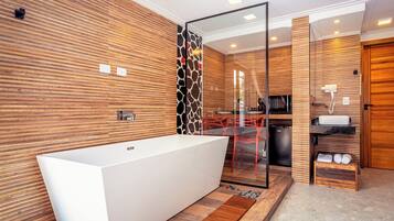 A modern bathroom with a large white bathtub, wooden panel walls, a glass shower enclosure, and a small wooden shelf with towels.