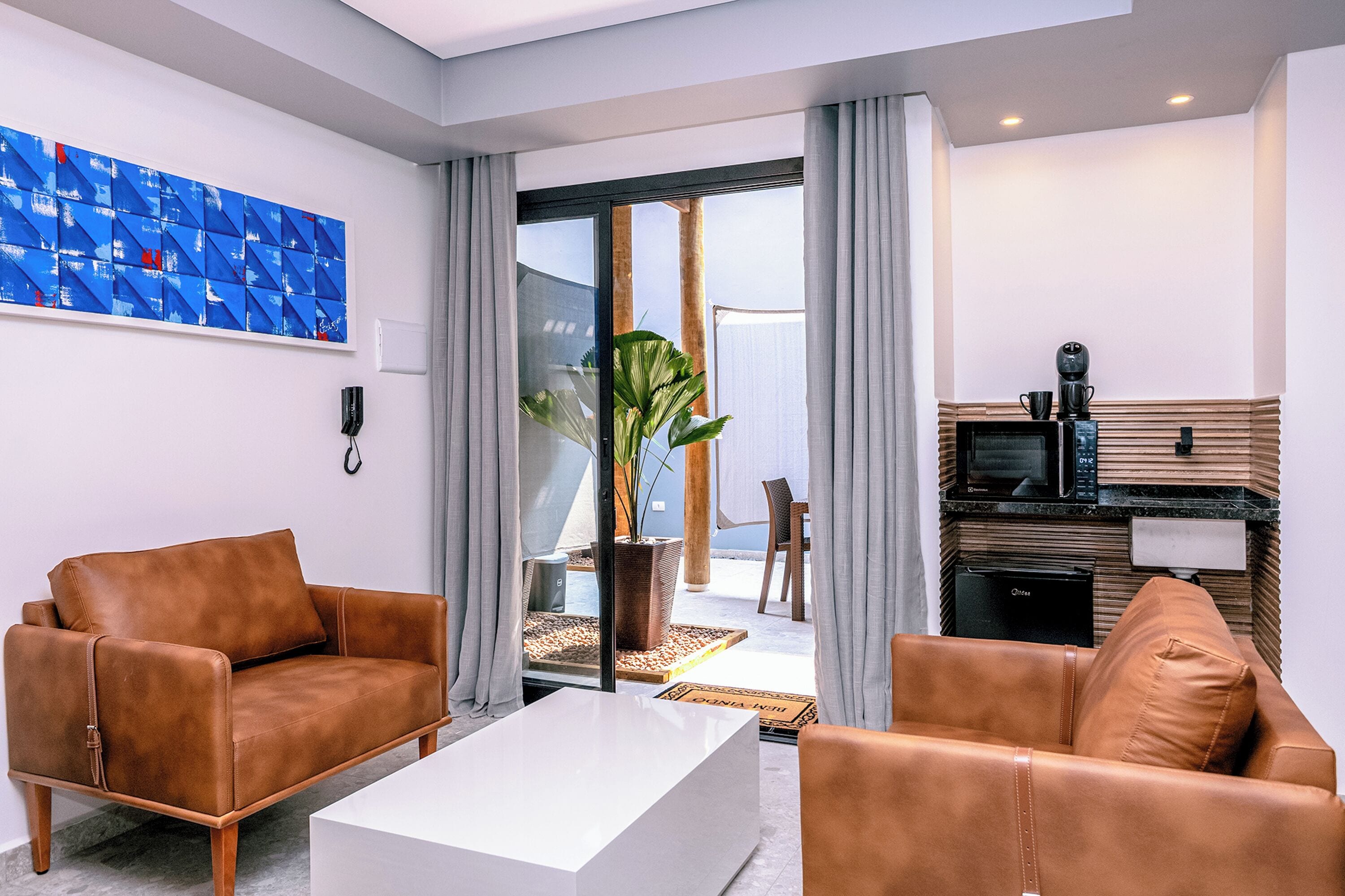 A modern living room with leather sofas, a white coffee table, and a kitchen area with a microwave.
