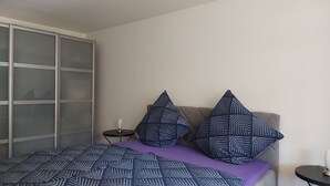 Un dormitorio con una cama, dos almohadas, una mesita de noche y un buró.