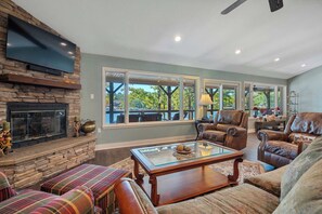A living room with a stone fireplace, leather furniture, and large windows.