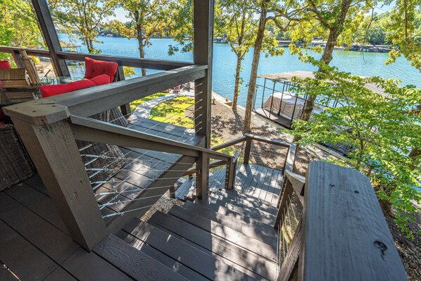 Una terraza de madera con vista a un lago, un banco acolchado rojo y una mesa de madera.