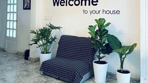 Ein Empfangsbereich mit einem 'Willkommen in Ihrem Zuhause'-Schild, einem gemusterten Sofa und Blumentöpfen.