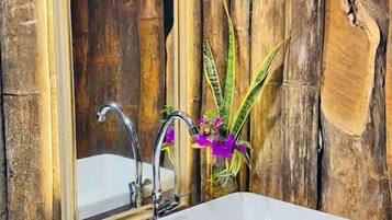 A bathroom with a white sink, two faucets, a mirror, and bamboo walls.