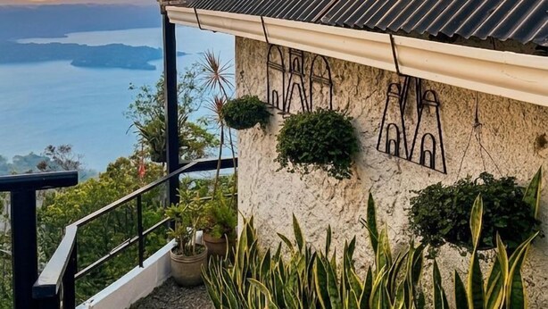 A staircase leading to a building with a corrugated metal roof, surrounded by plants and overlooking a body of water. - Bistro La Petite (San Francisco Chinameca)