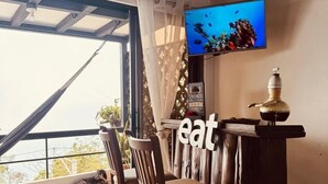 A room with a TV mounted on the wall, a bar counter, and a view through a large window. - Bistro La Petite (San Francisco Chinameca)