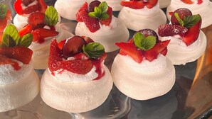 A glass plate with meringue-topped desserts garnished with strawberries and mint leaves. - Bistro La Petite (San Francisco Chinameca)