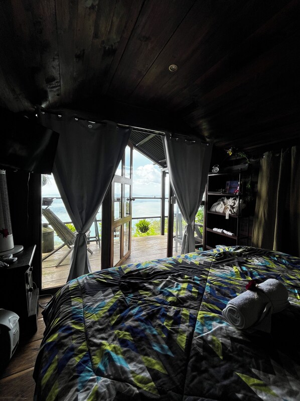 A bedroom with a bed, curtains, a window, and a view of the sea. - Bistro La Petite (San Francisco Chinameca)