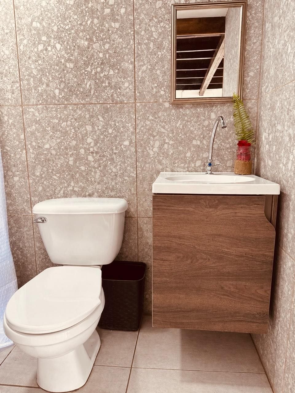 Et badeværelse med toilet, vask, spejl og en skraldespand.
