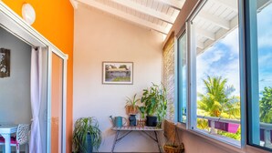 Ein Balkon mit Blumentöpfen, einem gerahmten Bild und Blick auf Palmen.