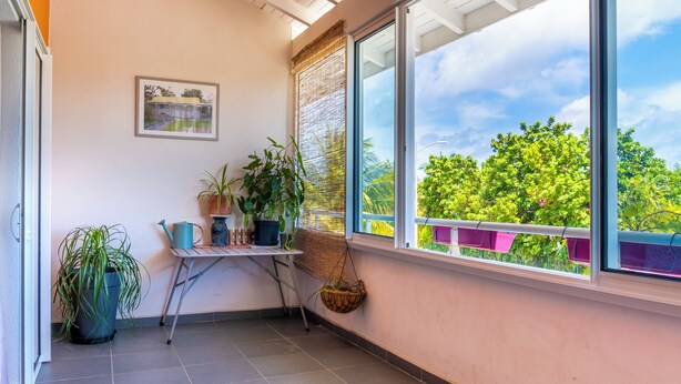 Ein Balkon mit Topfpflanzen, einem kleinen Tisch und einem Fenster mit Blick ins Grüne.