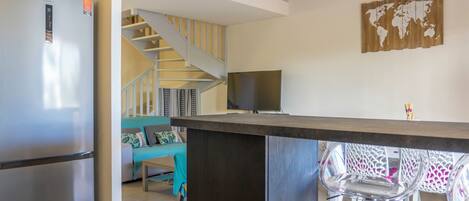 A modern kitchen with a built-in refrigerator, a dining area with a bar counter, and a staircase leading to an upper level.