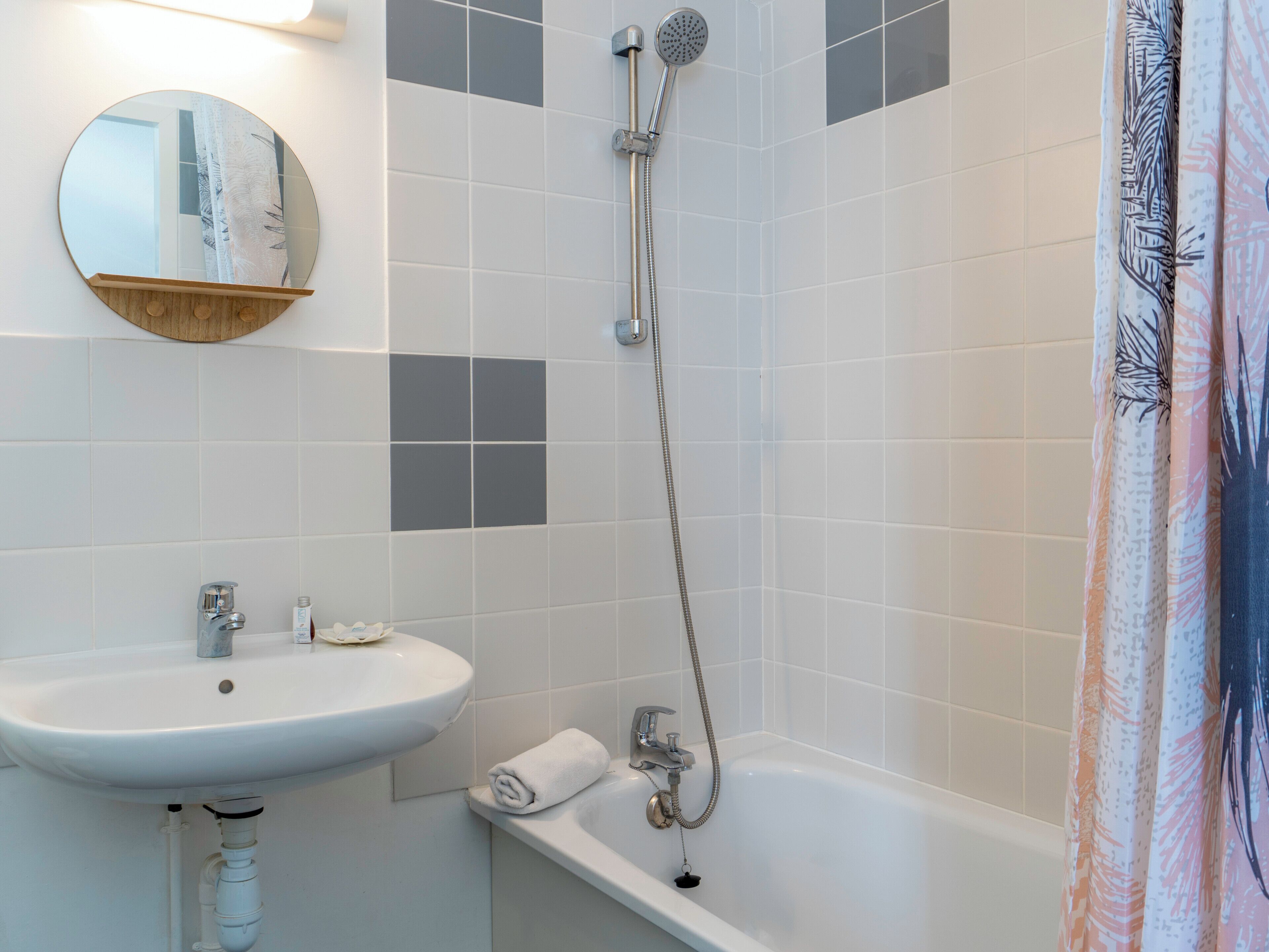 A bathroom with a white sink, a mirror, a shower, and a towel.