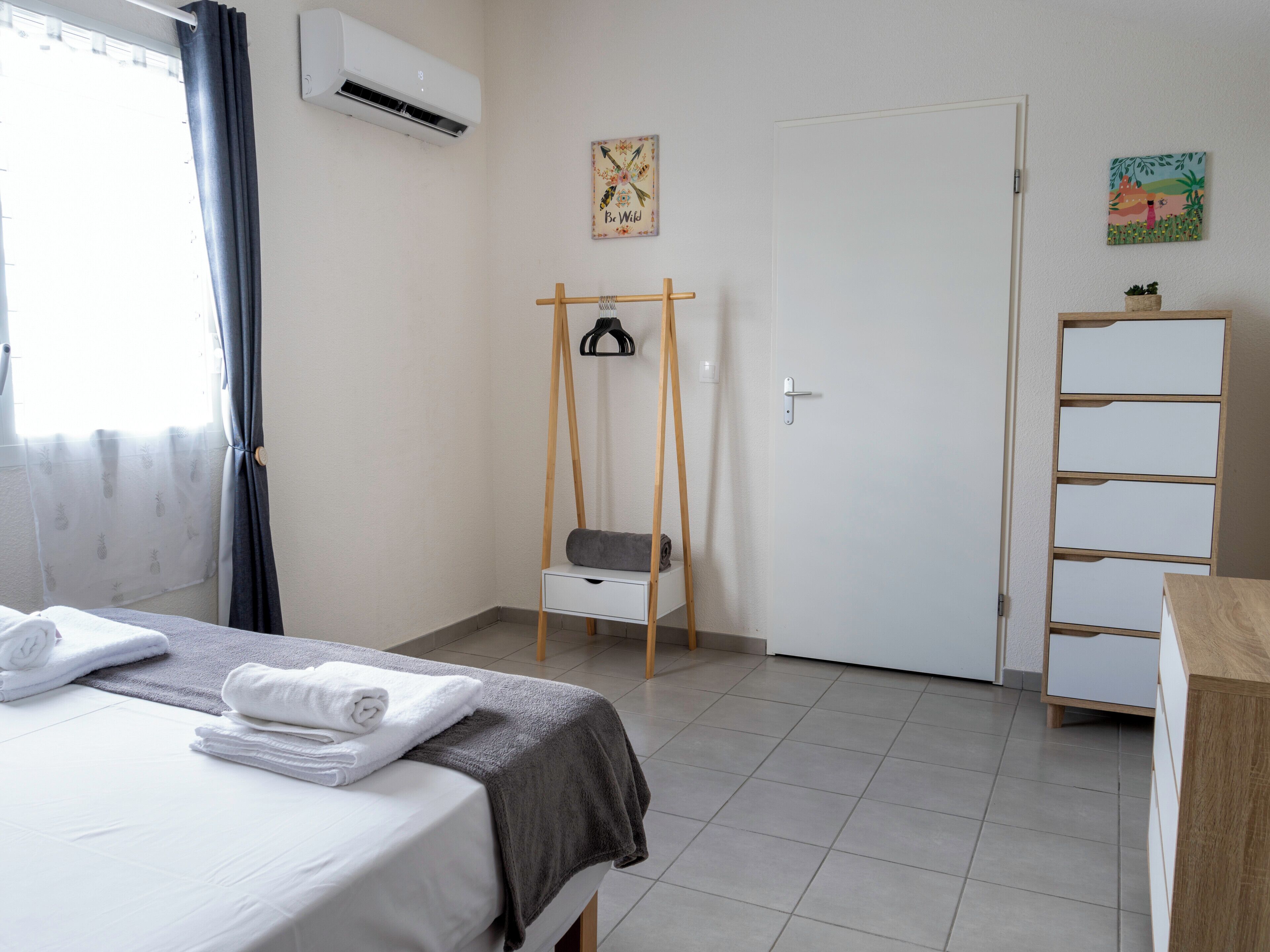 A hotel room with a bed, a small wooden chair, a white wardrobe, and a door with a picture on the wall.
