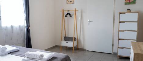A hotel room with a bed, a small wooden chair, a white wardrobe, and a door with a picture on the wall.