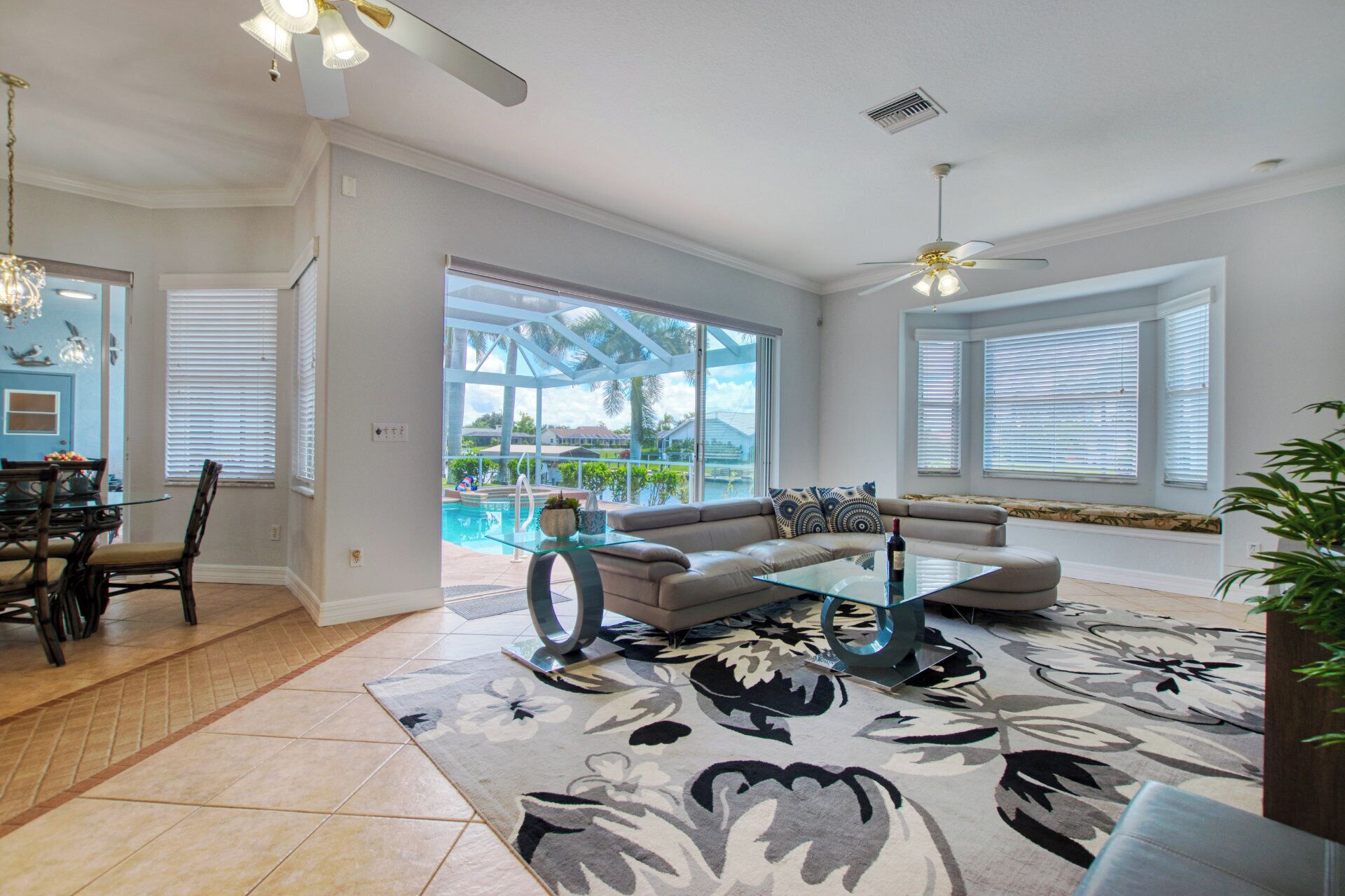 A spacious living room with a large glass coffee table, a beige sofa, and a view of a swimming pool.