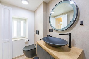 Moderni kylpyhuone, jossa on pyöreä peili, erillinen pesuallas ja wc-istuin.
