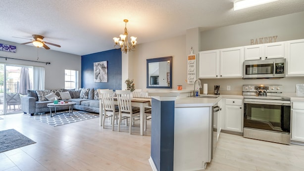 A modern kitchen with white cabinets, a built-in microwave, and an oven. There is a dining area with a table and chairs. - Townhome 7 Mi to Disney Parks: Resort Pool Access! (Kissimmee)