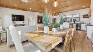 Un vaste espace de vie comprenant une table à manger en bois, un canapé gris et une cuisine à l’arrière-plan.