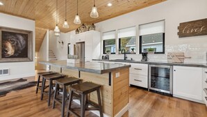 Une cuisine moderne dotée d’un îlot central, de tabourets de bar, de luminaires suspendus et d’une grande fenêtre.