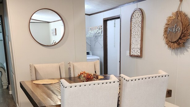 A dining area with a wooden table and four upholstered chairs, a round mirror, and decorative wall hangings. - The Rustic Hideaway  A Country Experience Horseback Riding and Fishing  (Cantonment)