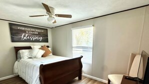 A bedroom with a bed, a ceiling fan, a window with blinds, and a motivational quote on the wall. - The Rustic Hideaway  A Country Experience Horseback Riding and Fishing  (Cantonment)