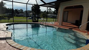 A clear swimming pool with a brick border, a metal ladder, and a covered area with a roof. - Spacious 3BR home with Heated Pool & WiFi! Great spot near beaches & shopping! (Port Charlotte)