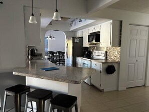 Une cuisine moderne avec un îlot central, des tabourets de bar et un coin repas à l’arrière-plan.