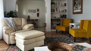 A living room with a beige sofa, a yellow armchair, a bookshelf, and a framed artwork. - Spacious 3BR home with Heated Pool & WiFi! Great spot near beaches & shopping! (Port Charlotte)