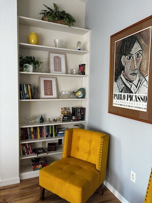 Une pièce comprenant une bibliothèque, une œuvre d’art encadrée de Pablo Picasso et un fauteuil jaune.