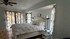 A bedroom with a bed, a nightstand, a lamp, a ceiling fan, and a window with curtains. - Spacious 3BR home with Heated Pool & WiFi! Great spot near beaches & shopping! (Port Charlotte)