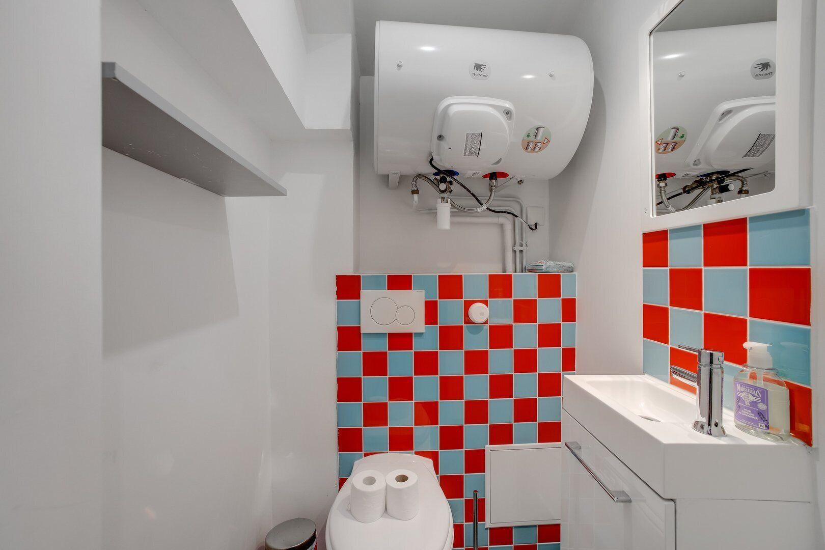 A modern bathroom with a white toilet, a sink with a mirror, and a shower with a white wall-mounted heater.