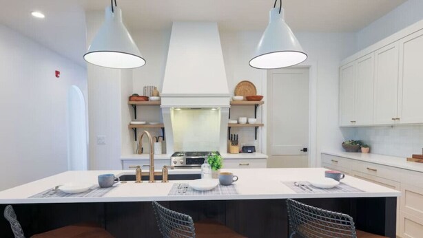 Une cuisine moderne dotée d’un grand îlot central, de luminaires suspendus et de tabourets de bar.