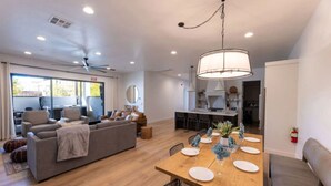 A modern living room with a sofa, dining table set for four, and a kitchen in the background. - Desert Haven Retreat Hot Tub Fire Pit Near Zion (Hurricane)