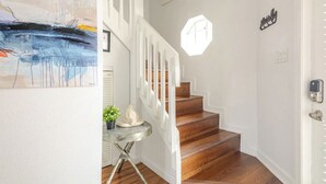 Una escalera con escalones de madera y barandillas blancas, una mesita con una planta y un cuadro en la pared.