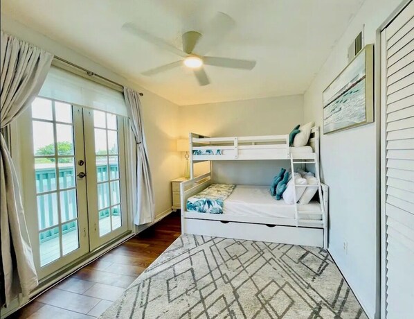 Une chambre avec un lit superposé, un ventilateur de plafond, une fenêtre avec des rideaux et un tapis.