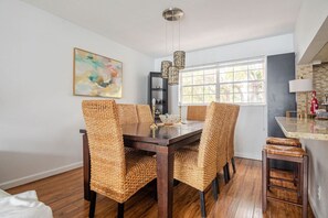 Uma sala de jantar com uma mesa de madeira escura, cadeiras de fibra, luminária pendente e janela com vista.