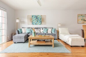 Una sala de estar con un sofá gris, un sillón blanco, una mesa de centro de madera y un tapete azul.