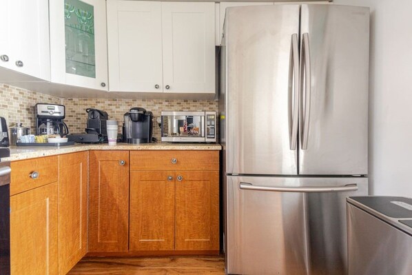 Una cocina con armarios de madera, un refrigerador de acero inoxidable, una cafetera y un microondas.