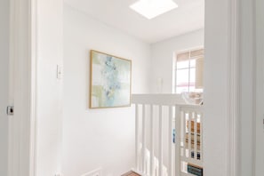 Un espacio interior blanco con barandilla blanca, un cuadro en la pared y una ventana con vistas.