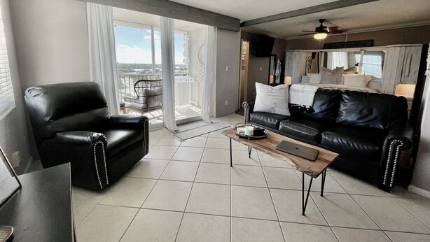 A modern living room with a black leather sofa, a black leather armchair, a wooden coffee table, and a large window offering a view of the city. - Penthouse condo, Gulf and Intercostal views, Bonita Beach and Tennis Club (Bonita Springs)