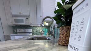 A kitchen with white cabinets, a stainless steel sink, a microwave, and a potted plant. - Penthouse condo, Gulf and Intercostal views, Bonita Beach and Tennis Club (Bonita Springs)
