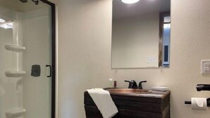 Ein Badezimmer mit Duschkabine aus Glas, einem Holzbadezimmerhocker und einem Spiegel darüber.