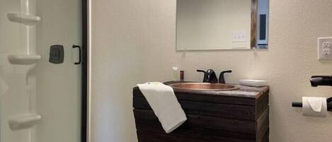 A bathroom with a glass shower enclosure, a wooden vanity with a sink, and a mirror above the vanity.