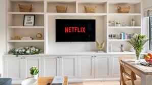 Un soggiorno con una TV a schermo piatto montata a parete, un tavolo da pranzo con sedie e una libreria con oggetti decorativi.