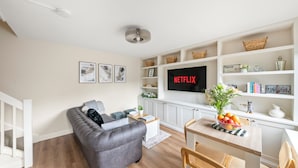 Un soggiorno moderno con un divano grigio, pavimento in legno, TV a parete e zona pranzo con tavolo e sedie.
