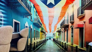 A narrow street with colorful buildings, a chair, and a star decoration. - Outdoor Pool with Bar-B-Q & Television, Indoor Pool Table, Indoor Bar, PS5, Etc. (Luquillo)